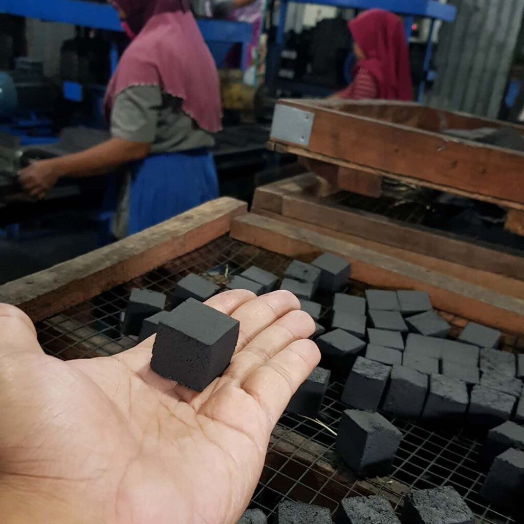 Hand holding a finished coconut charcoal briquette cube sourced through Indonesian supply networks